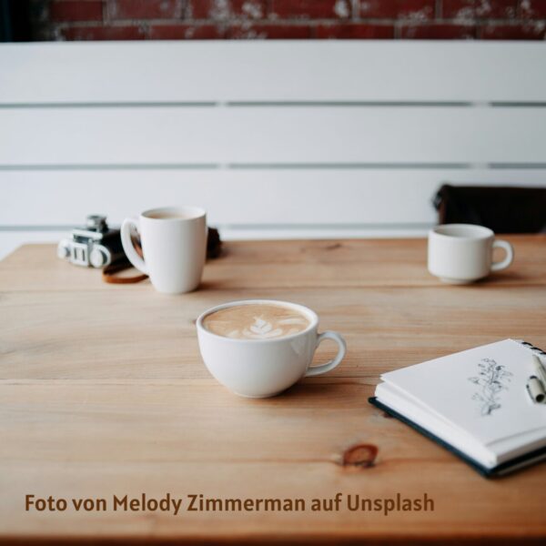Holztisch mit Kaffeetassen und Notizbuch in ruhiger Alltagsszene – Moment zum Innehalten und bei sich ankommen